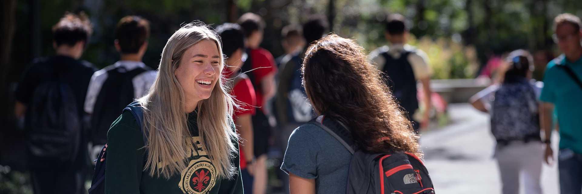 Photo of two Case Western Reserve University students talking outside, one facing the camera and smiling and the other with their back to the camera